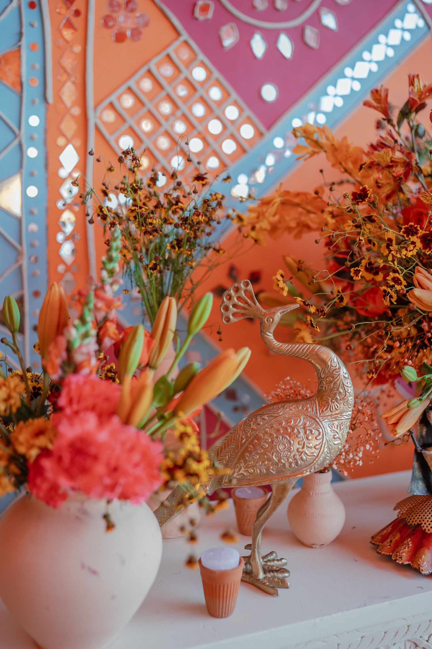 A series of white vases with orange and pink flower arrangements displayed against a coral-colored patterned wall.