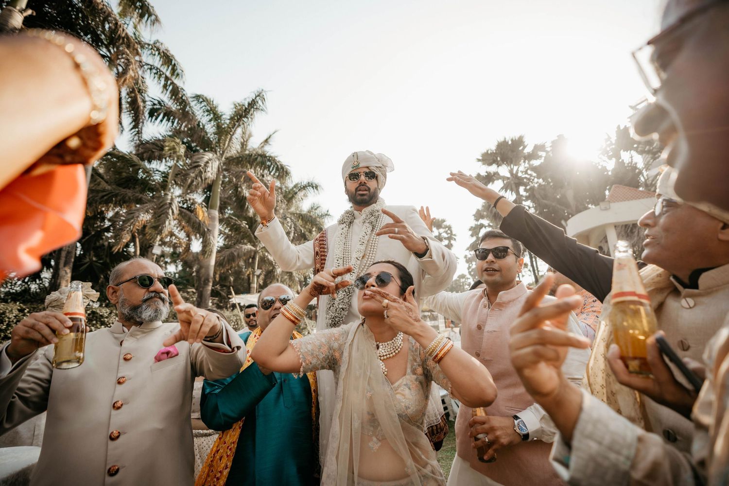 Wedding guests celebrate outdoors during golden hour while tossing rose petals in joyful celebration at a tropical venue.