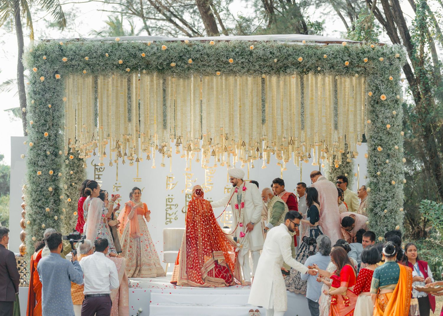 Traditional Indian wedding ceremony taking place under an outdoor mandap decorated with white flowers and fabric.