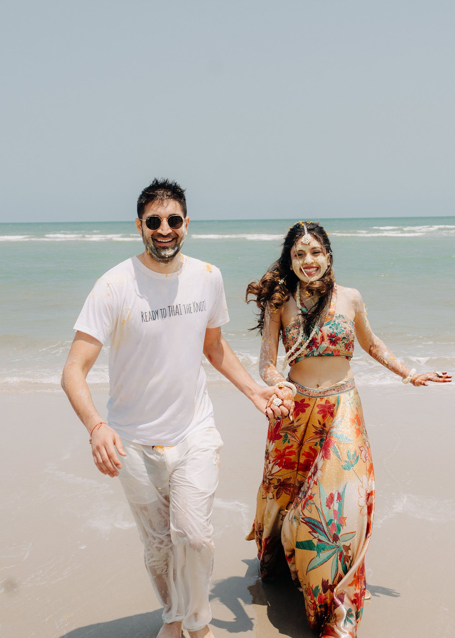 A couple enjoying a sunny day at the beach with ocean waves in the background, wearing casual summer attire.