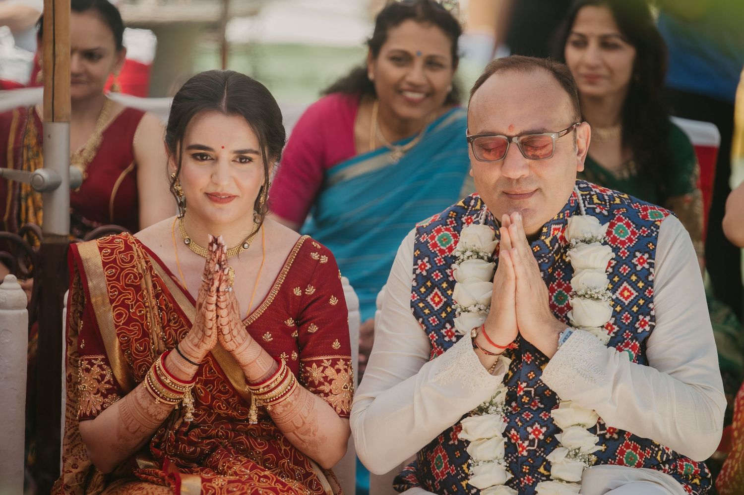 Two people wearing traditional Indian attire press their hands together in prayer position at a cultural celebration.