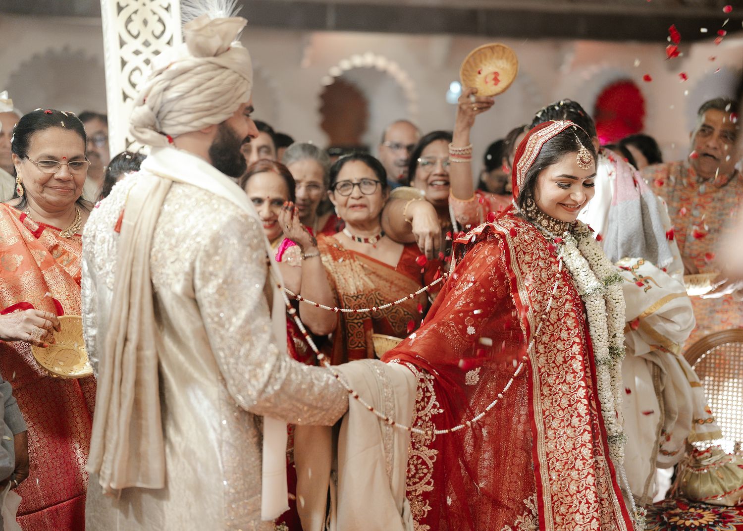 Bride and groom exchanging garlands during a traditional Indian wedding ceremony with guests celebrating around them.