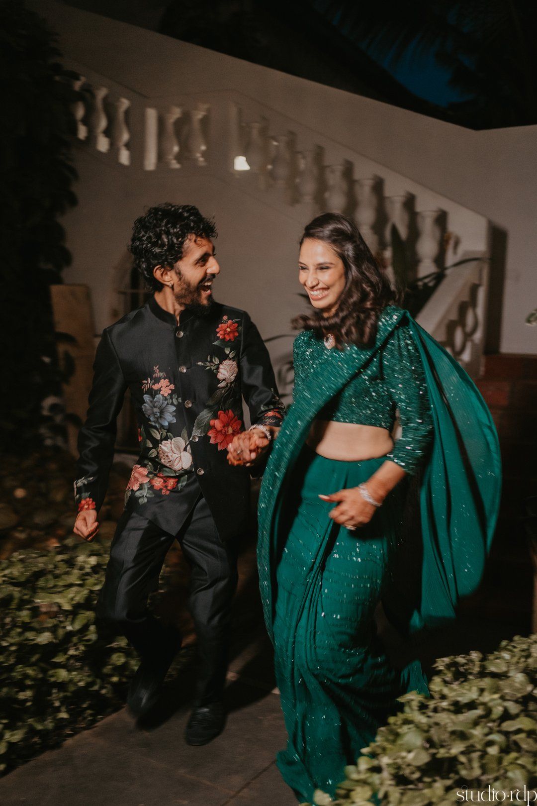 Couple in elegant emerald green and black floral outfits sharing romantic moments on outdoor steps.
