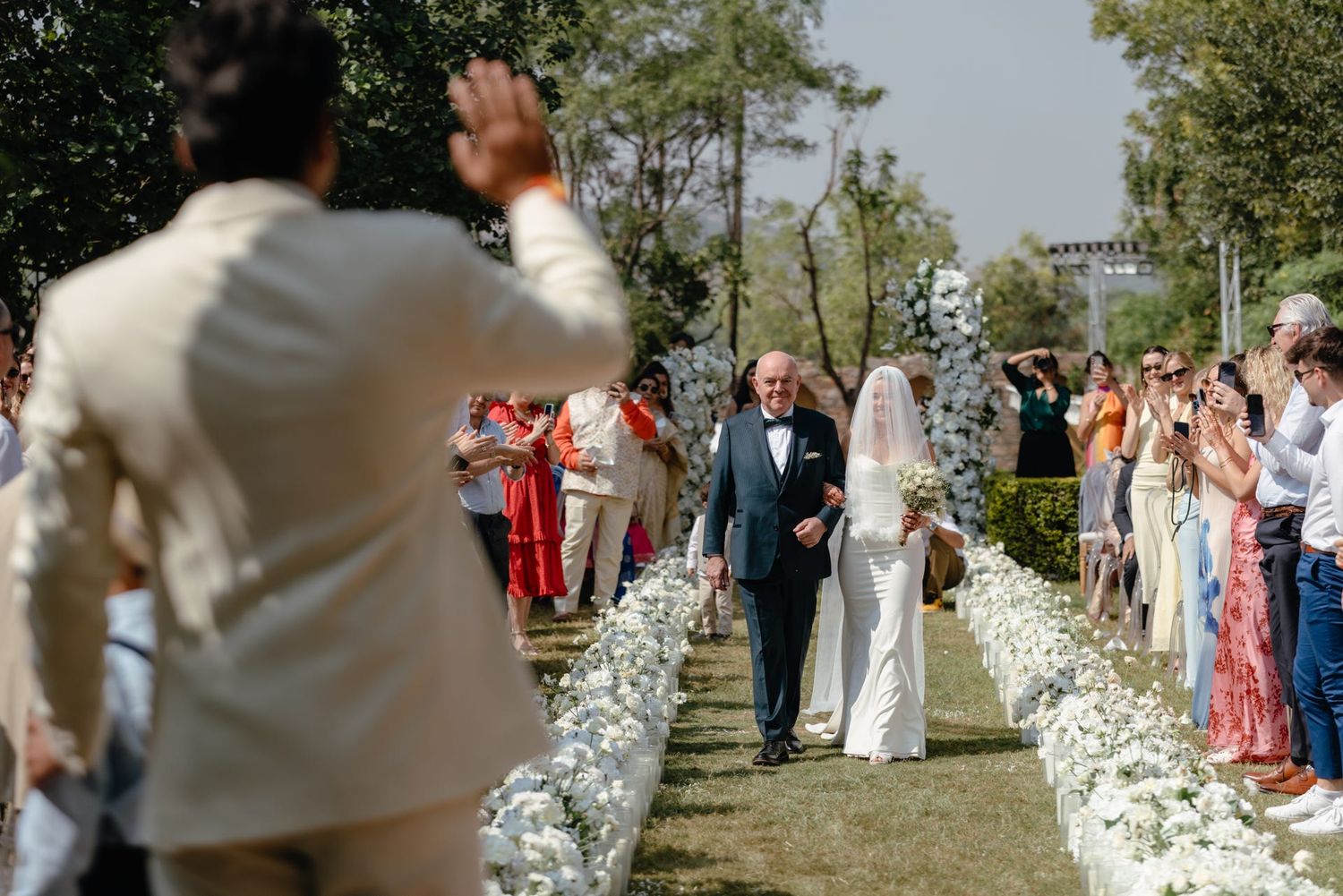 Wedding ceremony setup with white flower petals lining the aisle and guests seated outdoors.