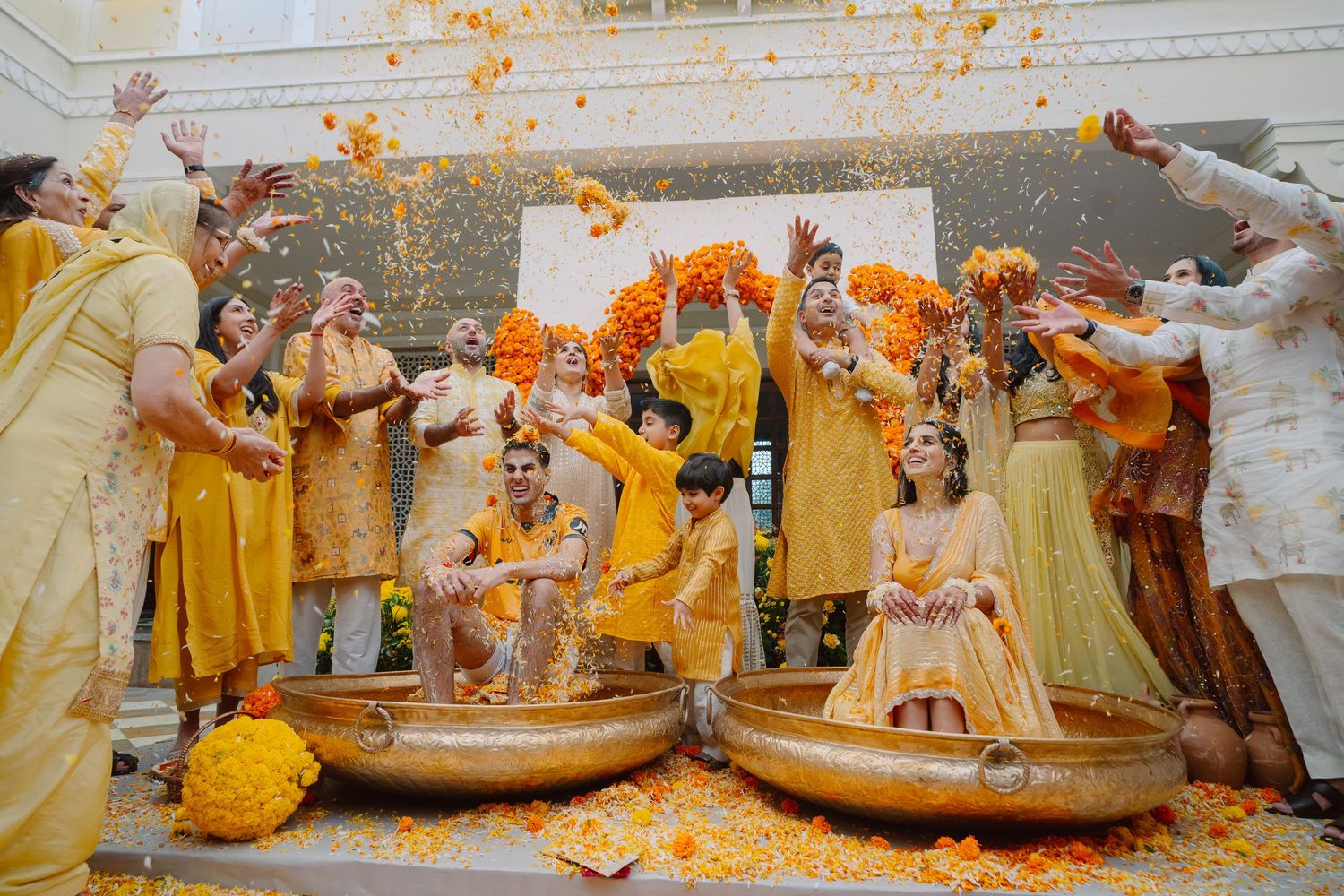 Festive Indian wedding celebration with guests throwing yellow powder amidst traditional decorations.