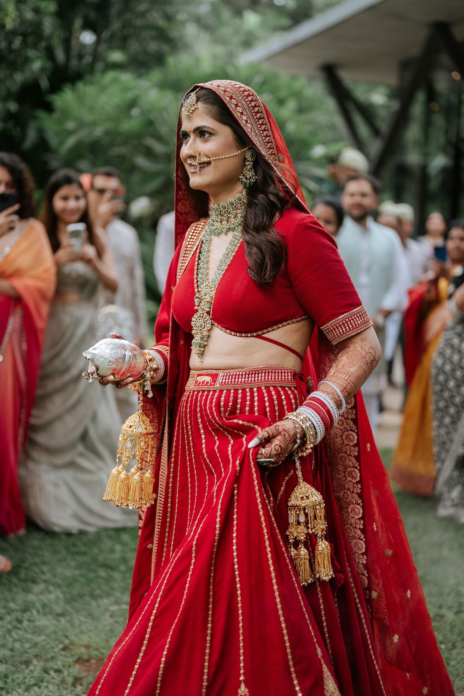 A bride in a stunning red lehenga with gold embroidery and traditional jewelry walks during her Indian wedding ceremony.