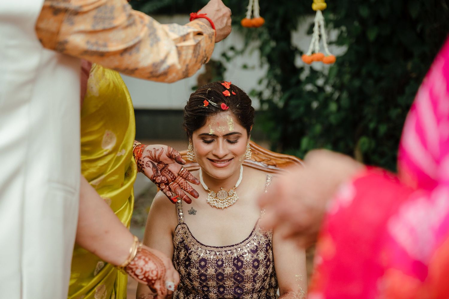 Indian bride in embroidered purple lehenga with mehndi hands receives blessings during traditional Hindu wedding ceremony.