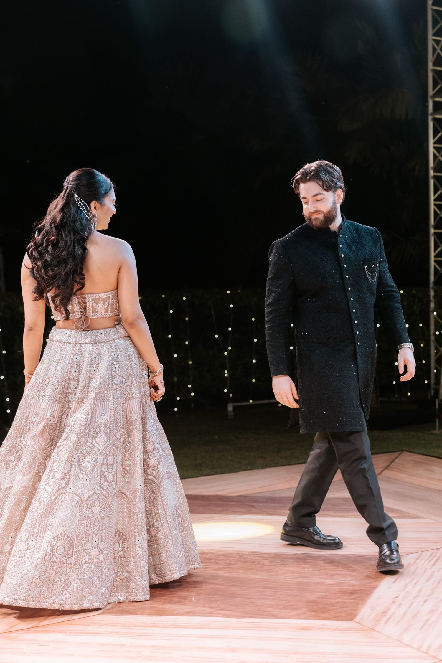 Couple shares first dance at Indian wedding, bride in ivory lehenga, groom in black sherwani.