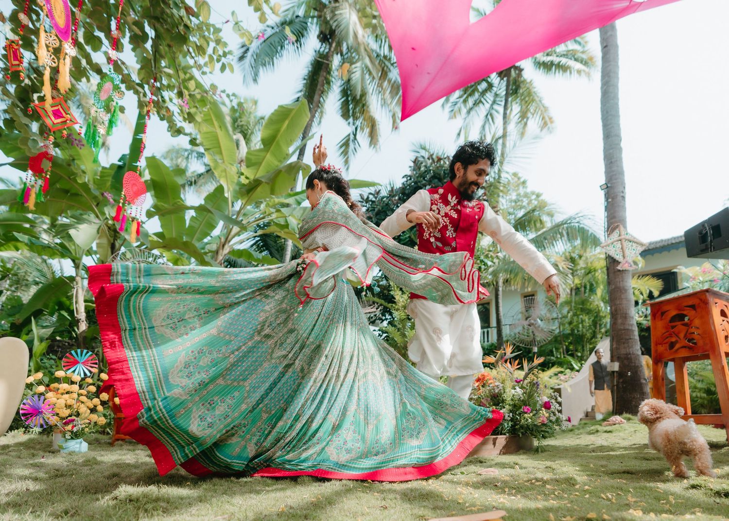 Couple dancing in traditional Indian attire at an outdoor wedding celebration surrounded by tropical greenery.