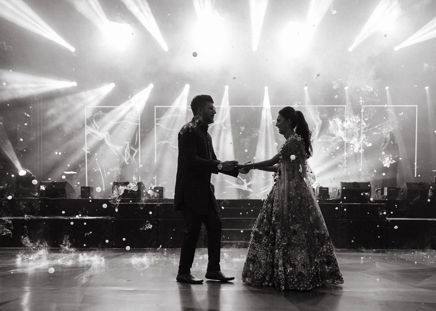 Black and white silhouette of two dancers on a stage with dramatic backlighting and sparkling effects.