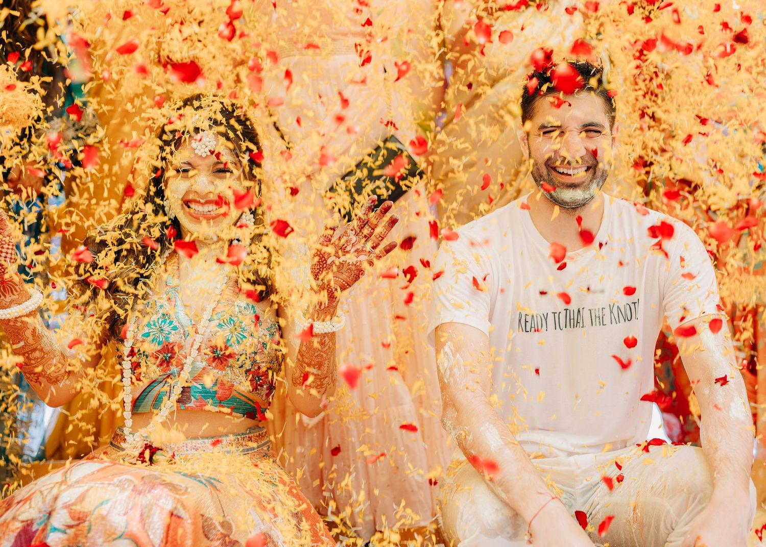 Couple celebrating with red and gold confetti showering over them in a joyful outdoor celebration scene.