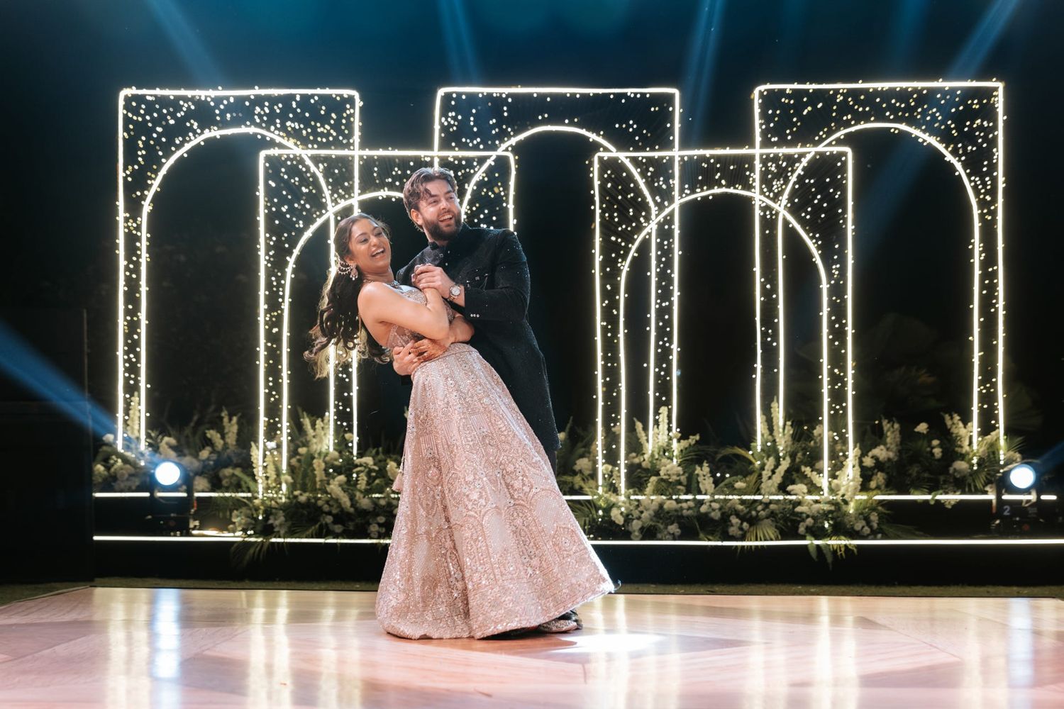Couple sharing first dance at wedding reception with elegant glowing arch backdrop and sparkling lights.