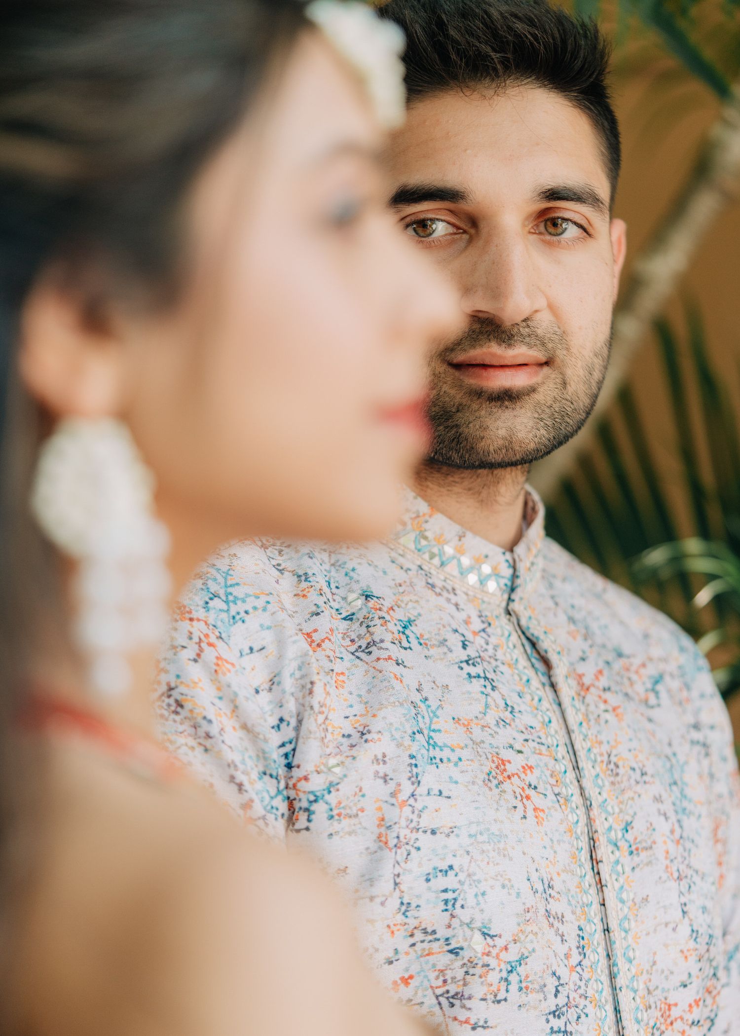 Close up profile portrait against green tropical foliage wearing a floral patterned shirt.