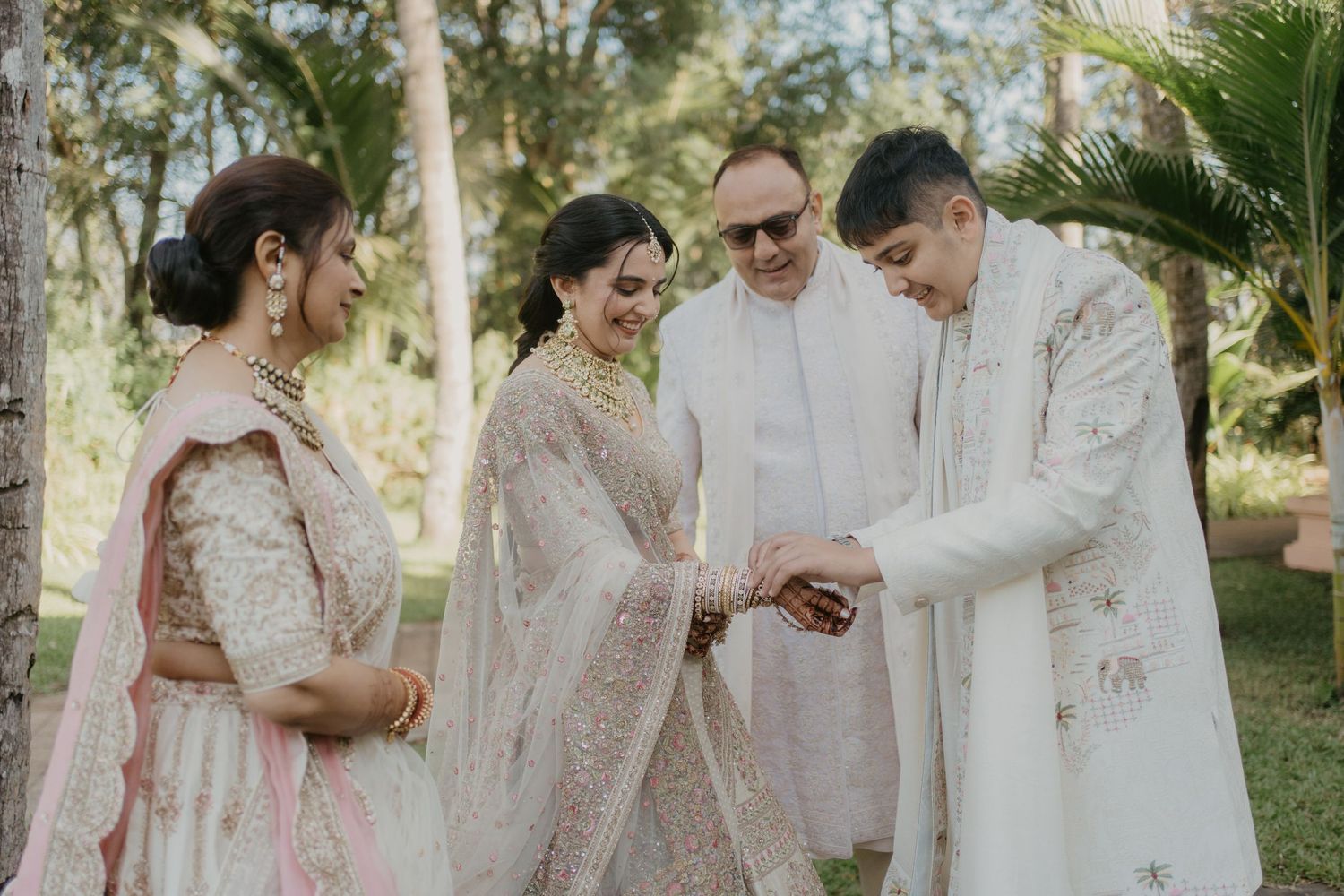 A group in traditional Indian wedding attire share a joyful moment together outdoors in a garden setting.