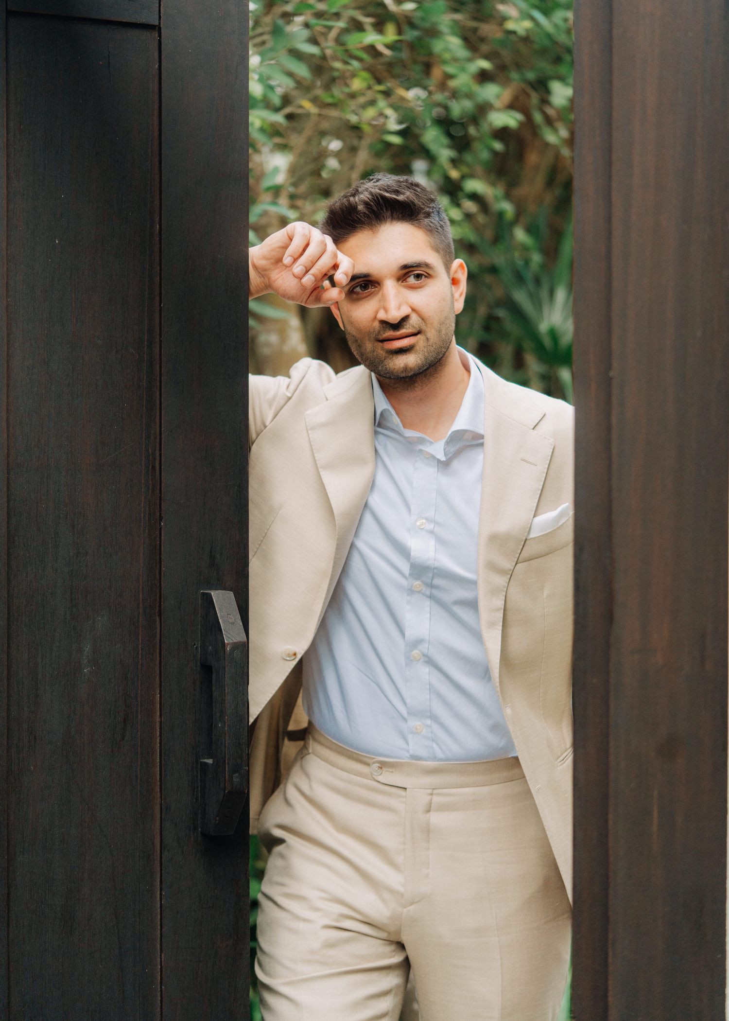 A series of four similar photos showing a person in a beige suit and light blue shirt posing playfully between dark columns.