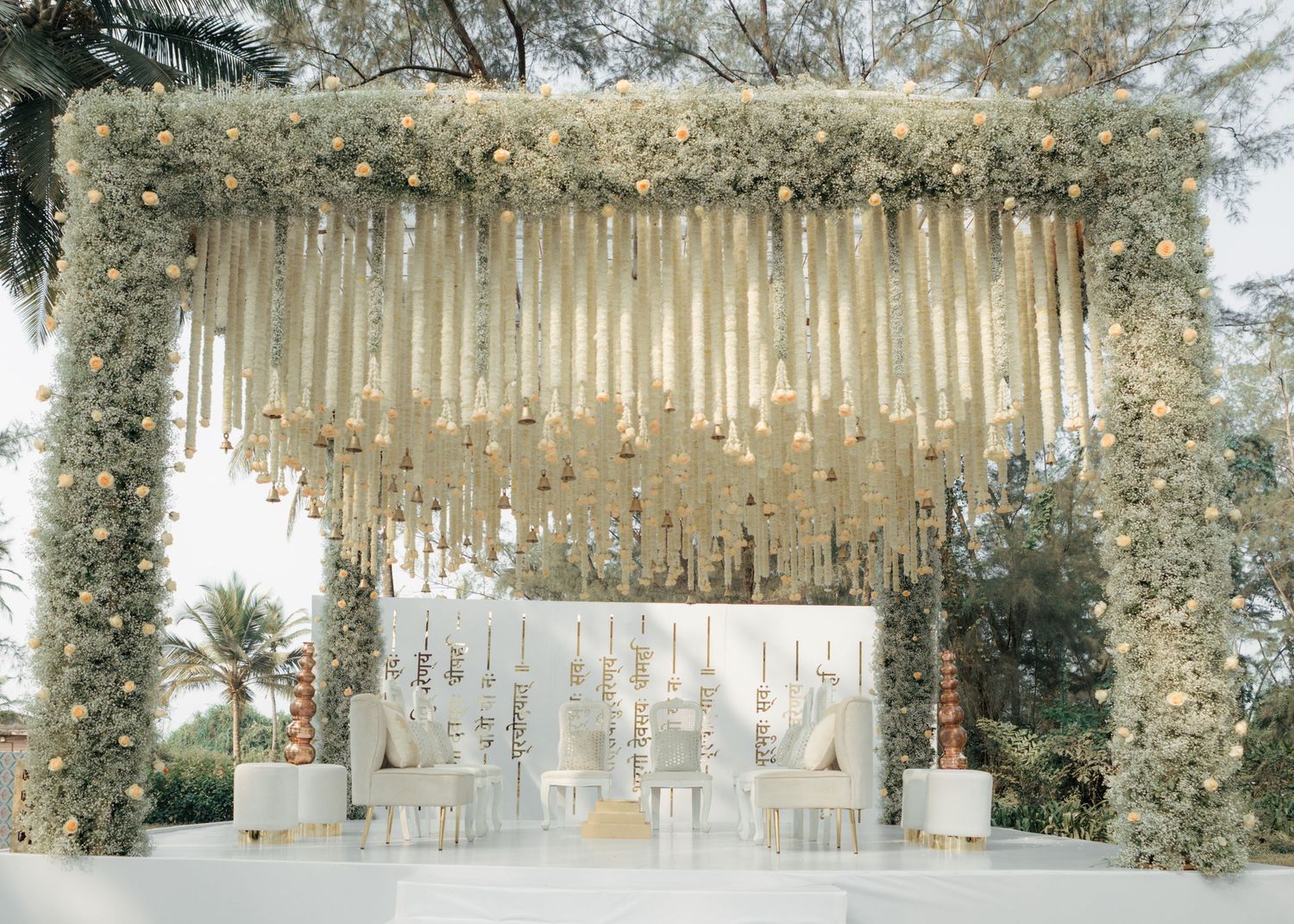 An elegant white wedding arch decorated with suspended glass tubes and delicate floral arrangements creates a dreamy ceremony space.