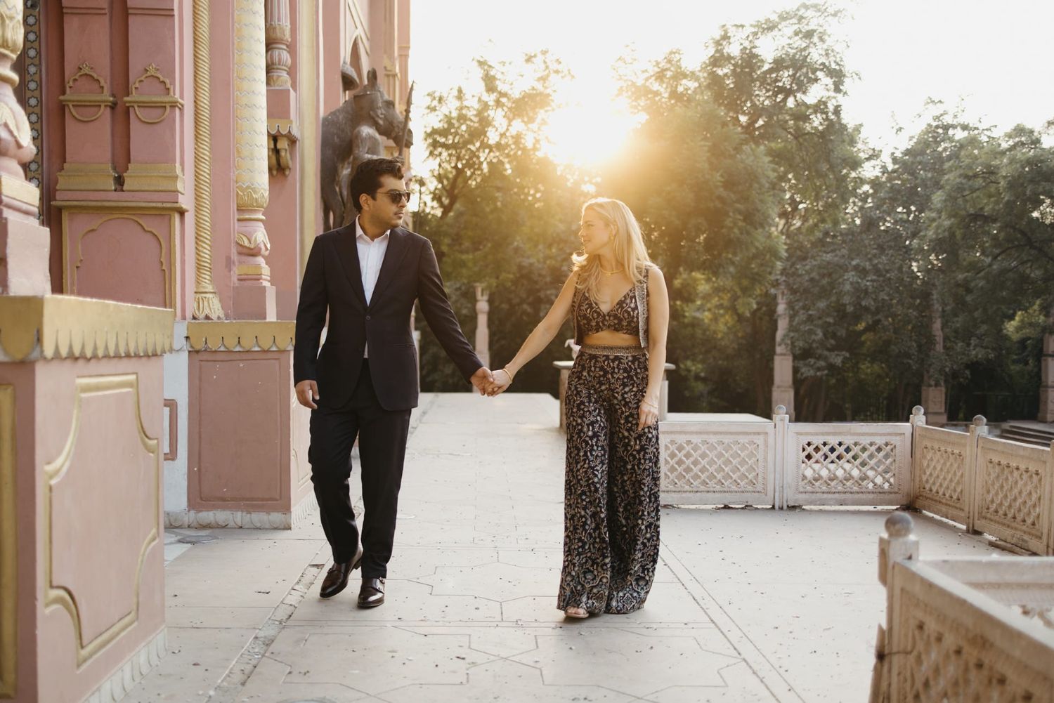 Silhouettes of a couple walking during sunset against ornate palace architecture.