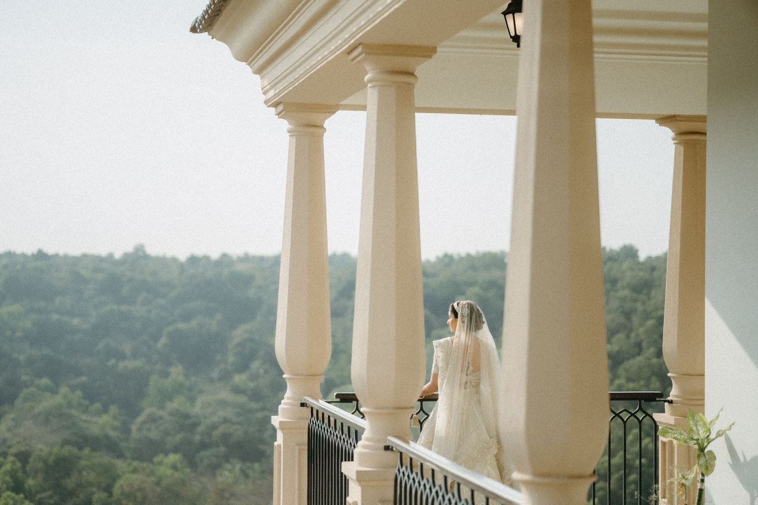 Elegant wedding dress styled between white columns on a scenic balcony with lush greenery, photographed by Studio RDP wedding photographers.