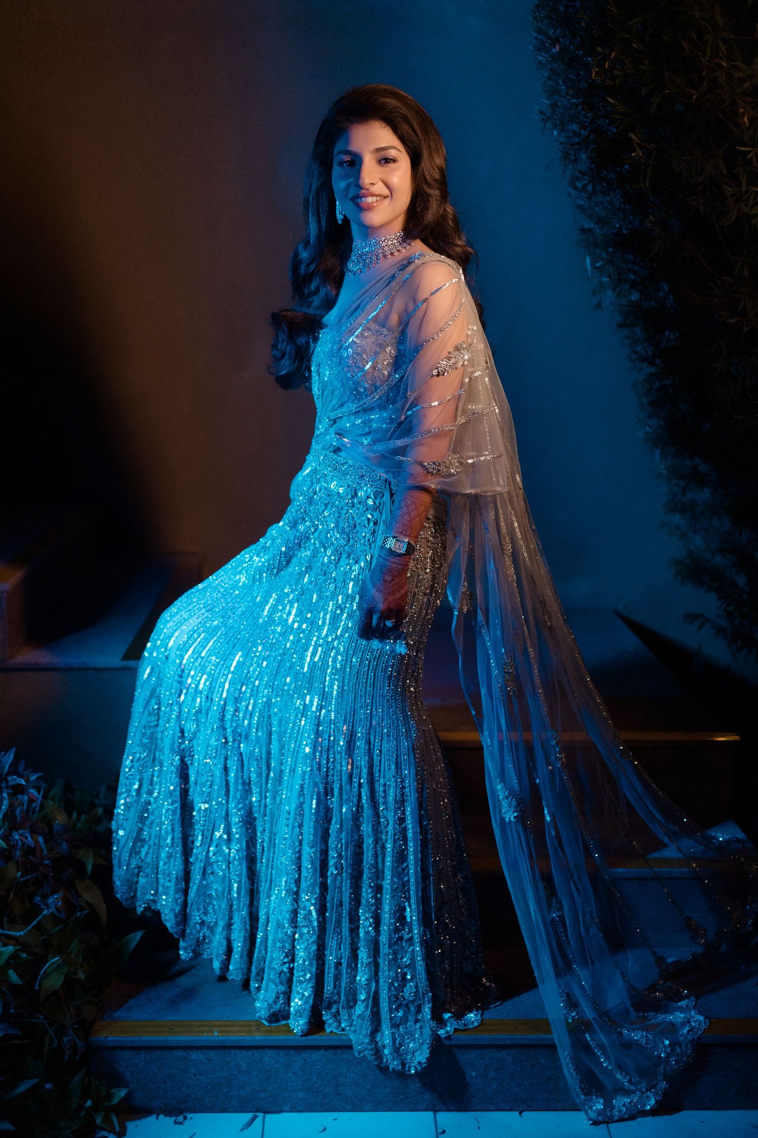 A figure in a sparkly blue dress and sheer cape poses dramatically against a dark background in a series of photos.