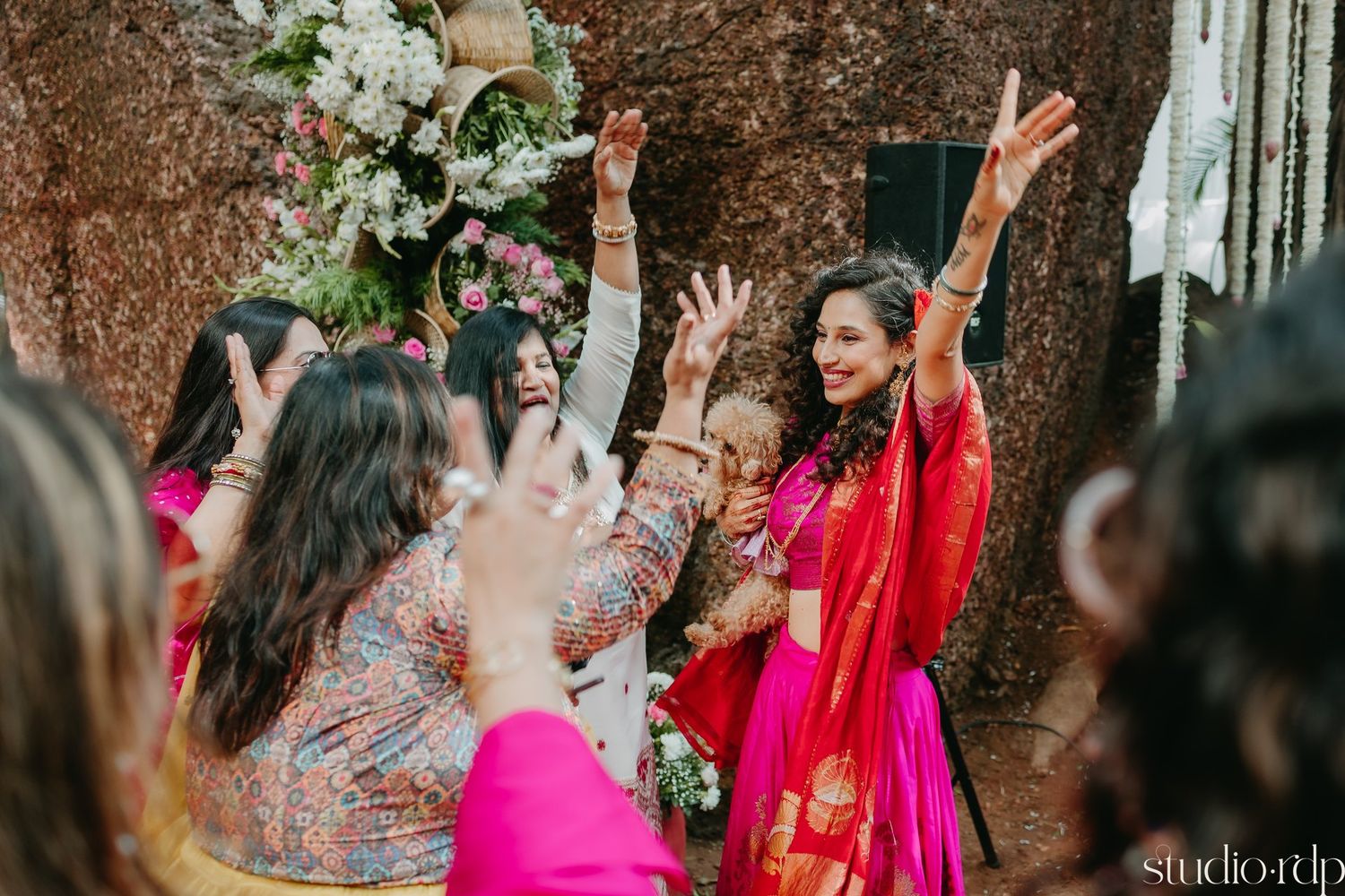 Wedding celebration with guests dancing and raising hands in joy amidst floral decorations.