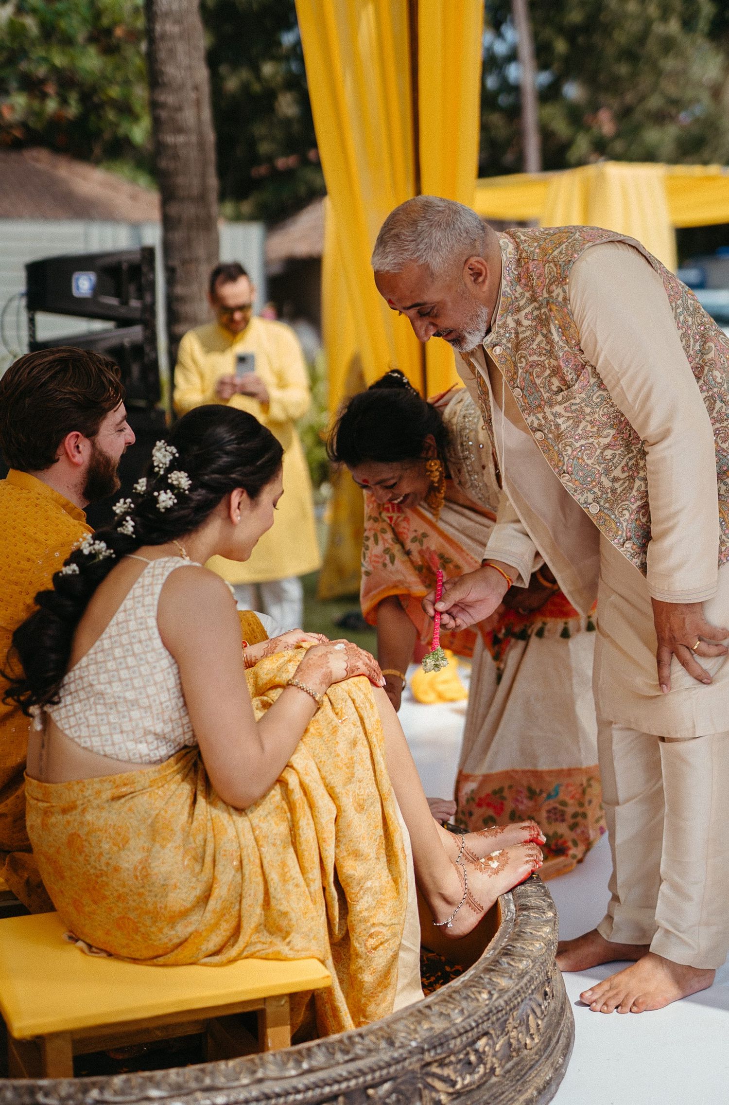 Elder applying haldi ritual to bride in yellow saree at traditional Indian wedding ceremony.