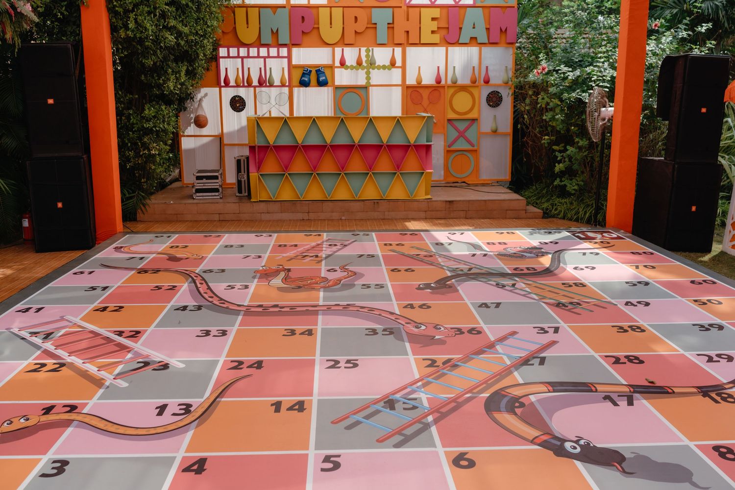 Large colorful outdoor board game setup with numbered squares and a decorated booth displaying 'Jump Up' signage in the background.