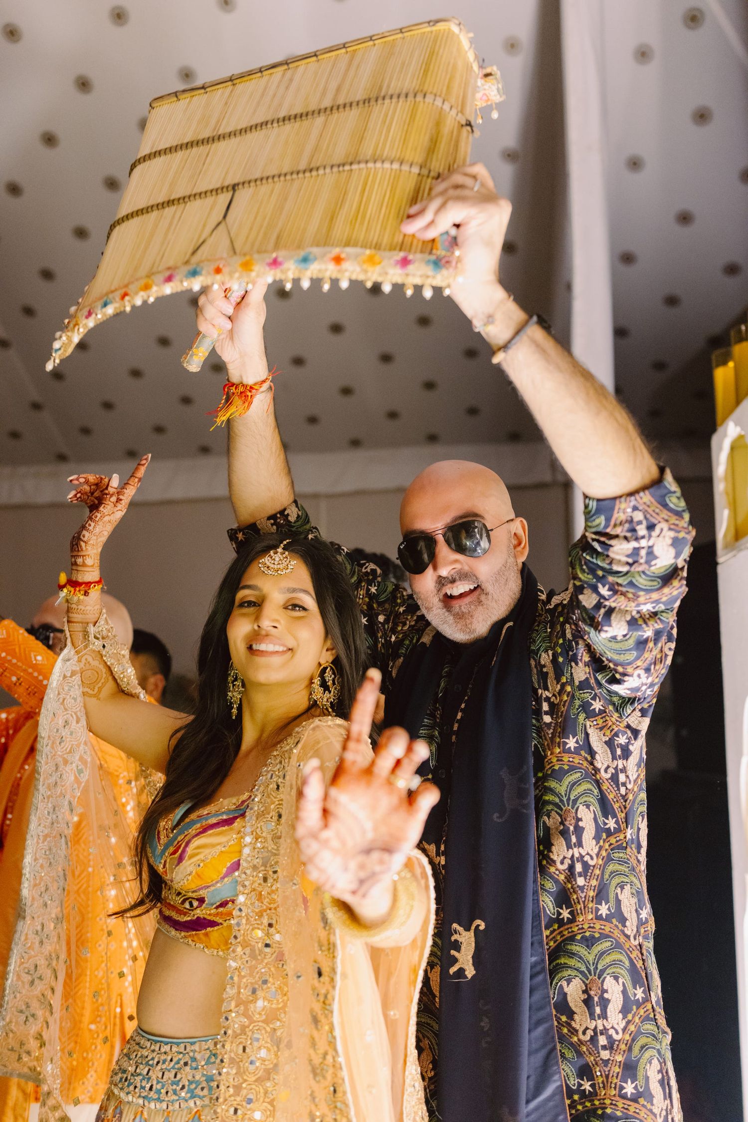 Wedding guests celebrate with raised arms and festive decorations during an Indian ceremony.
