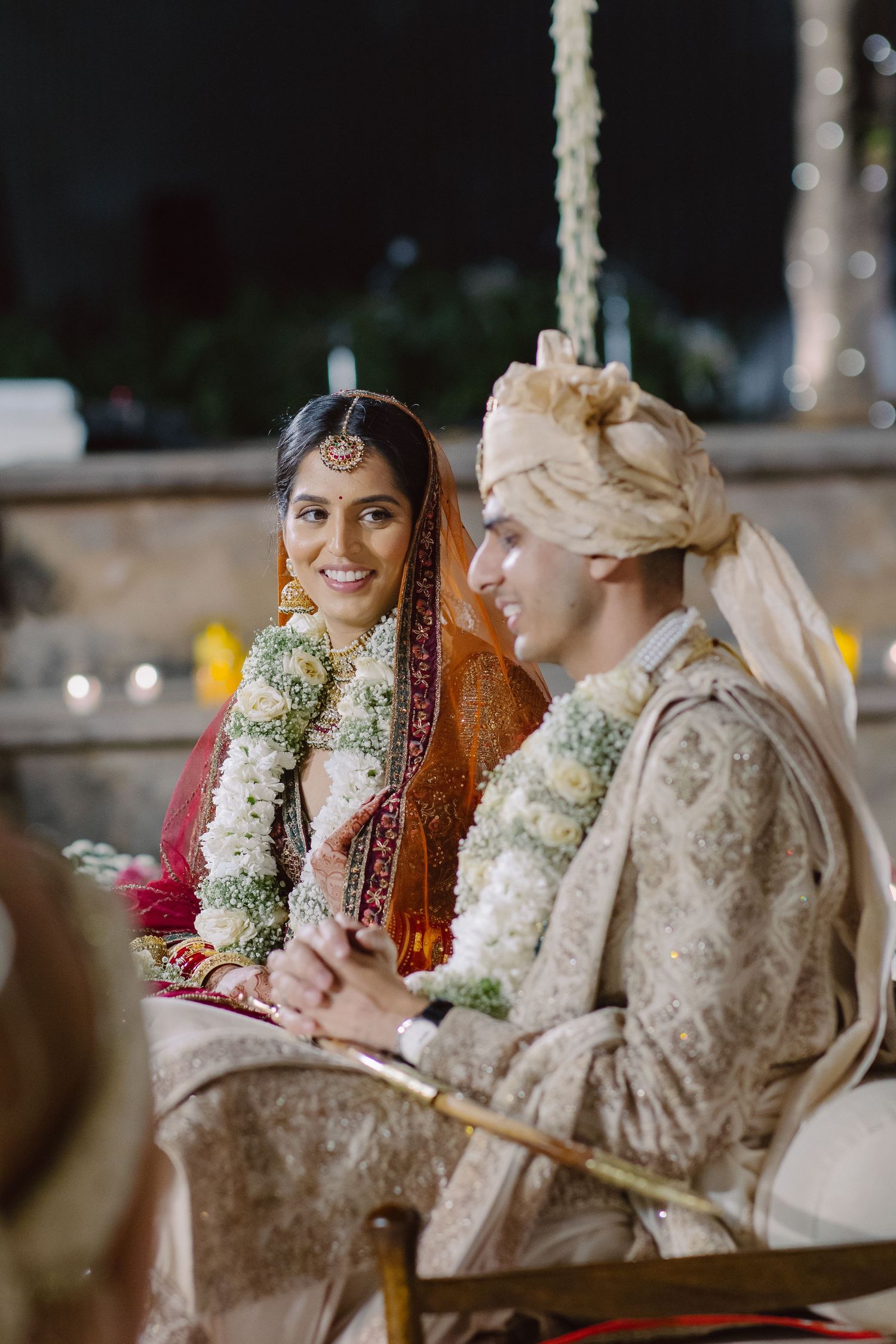 Traditional Indian wedding ceremony with couple seated under decorative floral mandap.