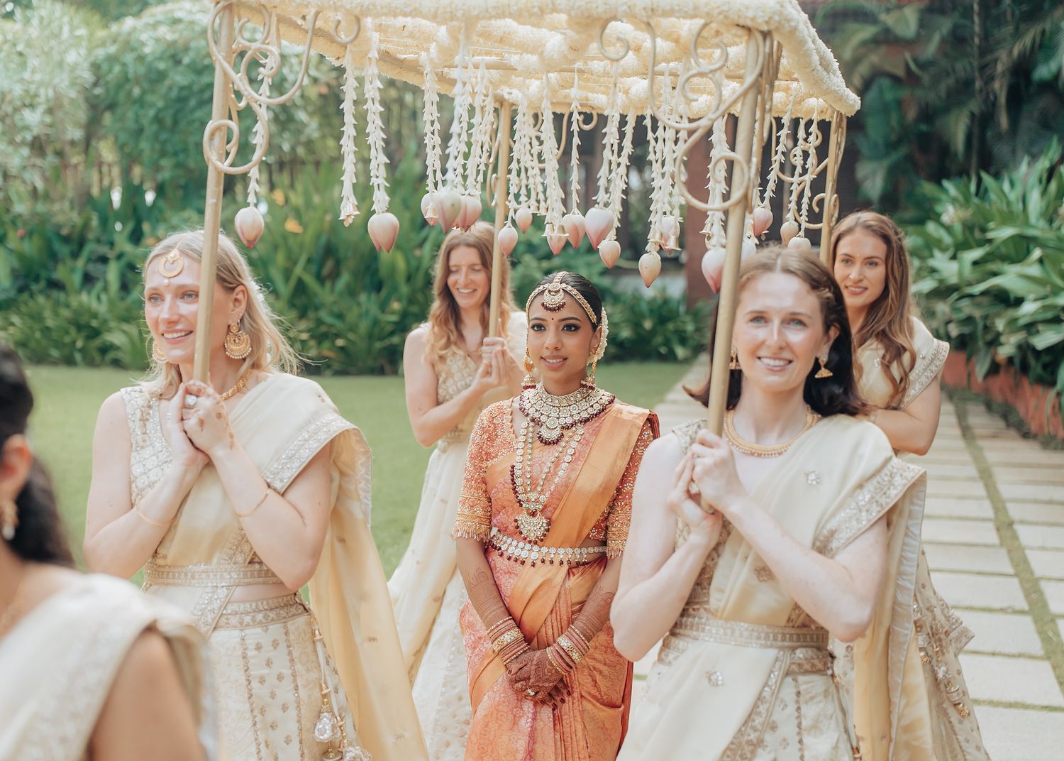 Wedding party in mix of traditional and Western attire gathered on outdoor garden path.