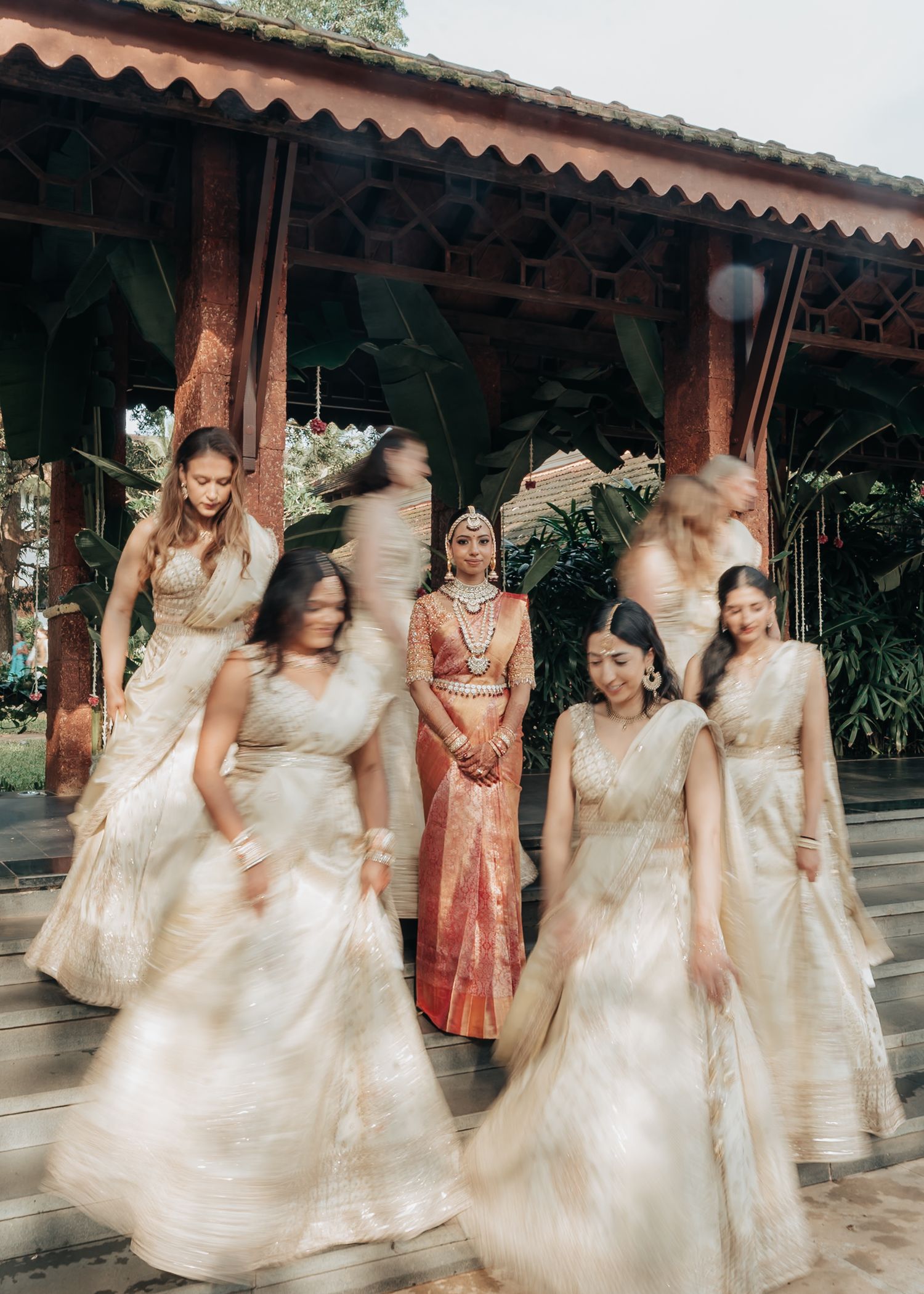 Group of bridesmaids in flowing cream-colored dresses twirling under a covered walkway.
