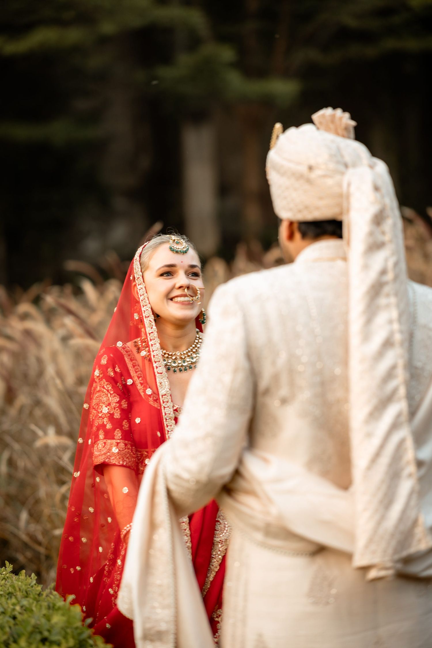 Wedding couple in traditional Indian attire share a joyful moment against a natural outdoor backdrop.