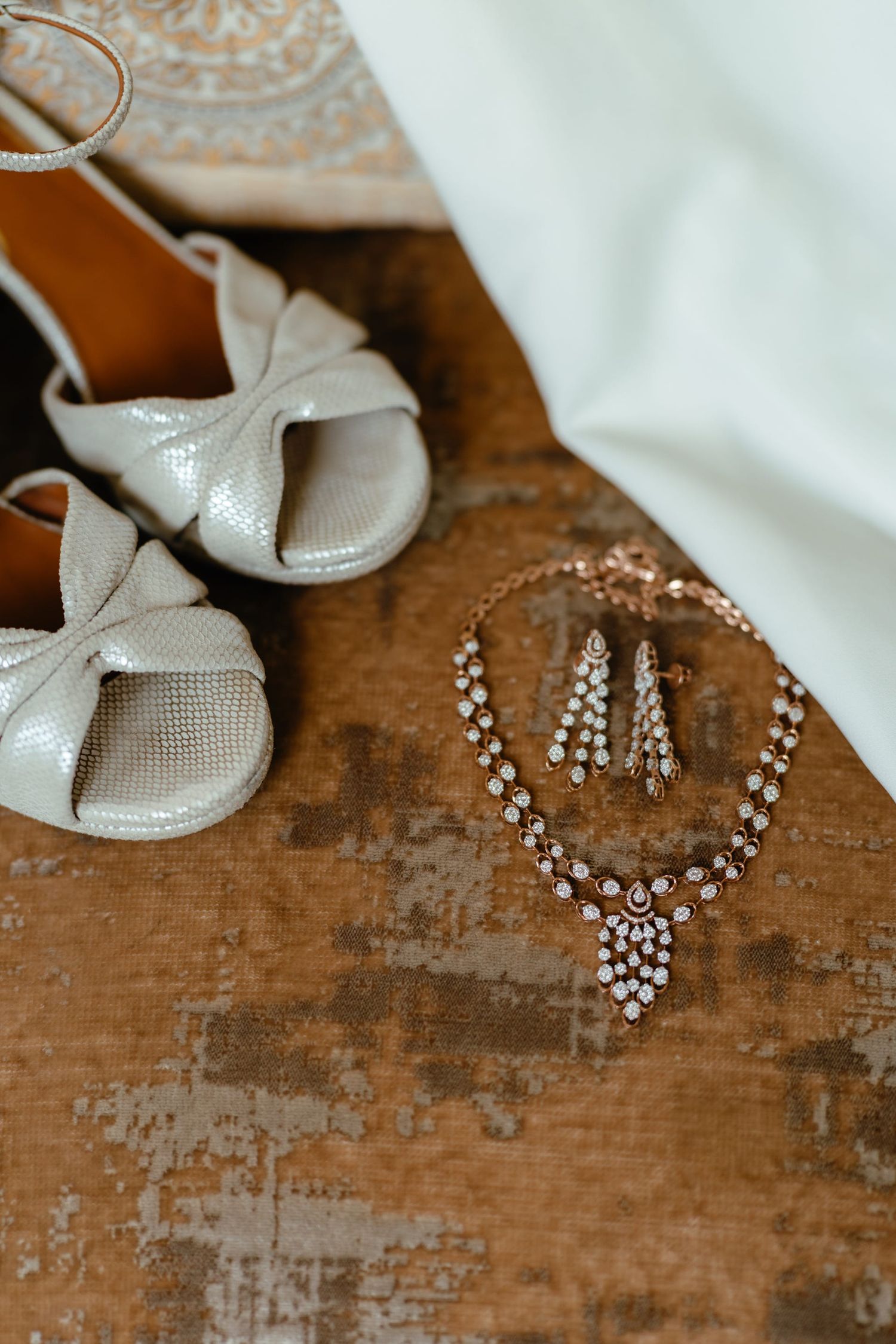Wedding accessories including white shoes and crystal jewelry arranged on rustic wooden surface.