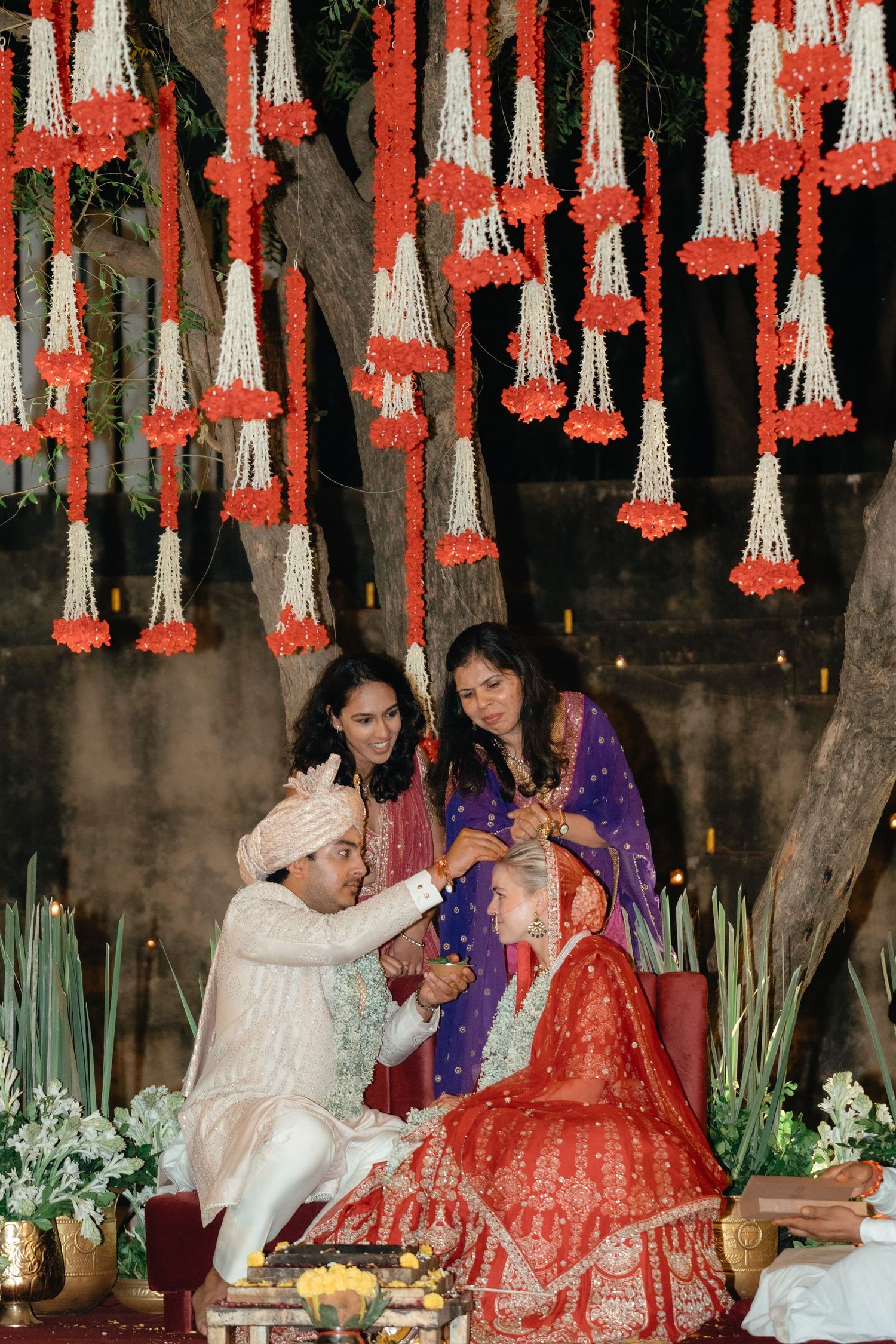 Wedding ceremony under hanging red and white floral decorations during a traditional Indian ritual.