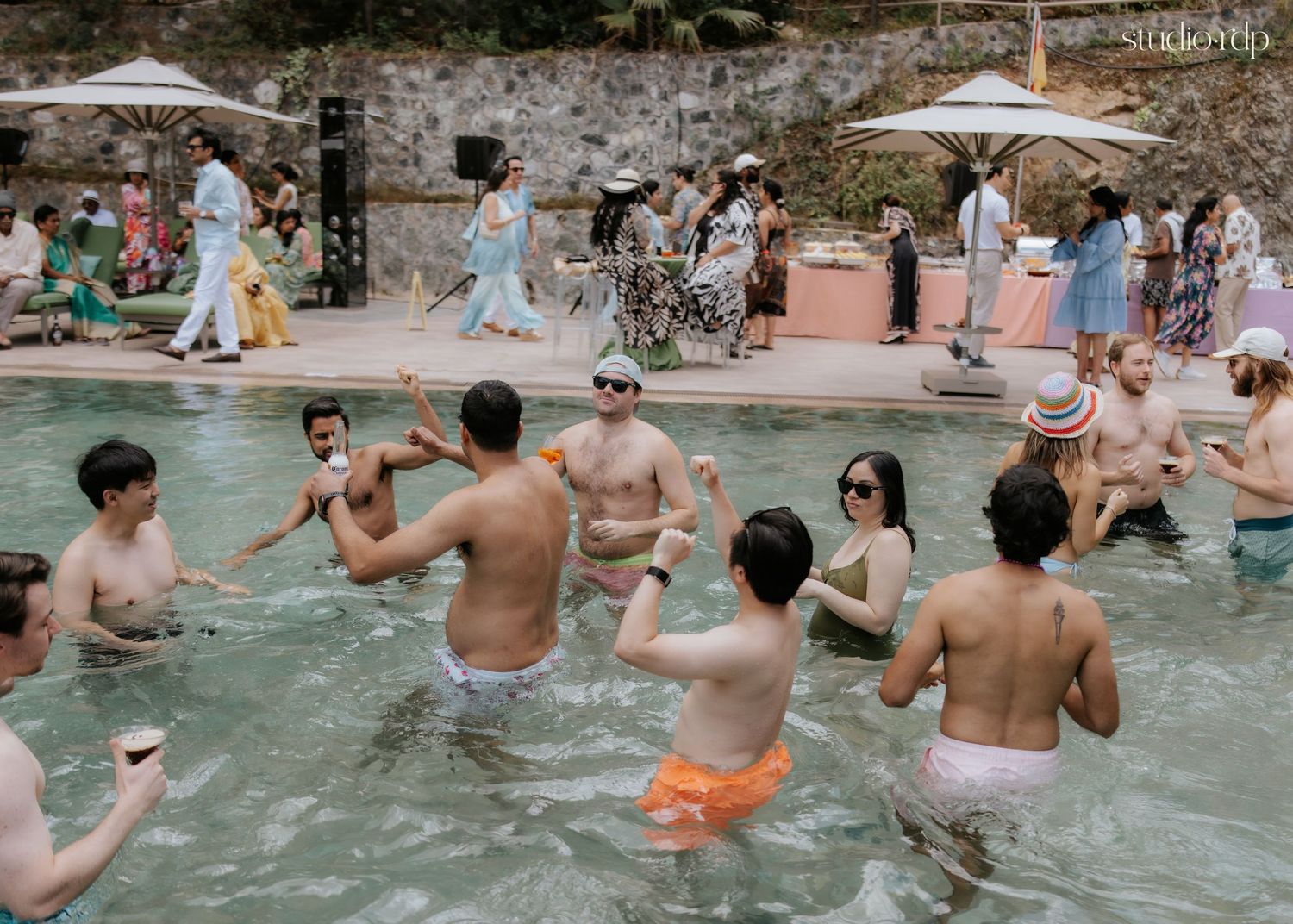 Guests dancing and socializing in an outdoor pool at a lively summer party surrounded by onlookers.