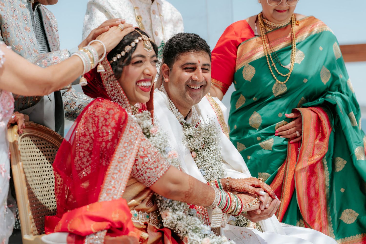 Joyful Indian bride and groom laughing during traditional Hindu wedding ceremony, bride in red saree with floral garlands.