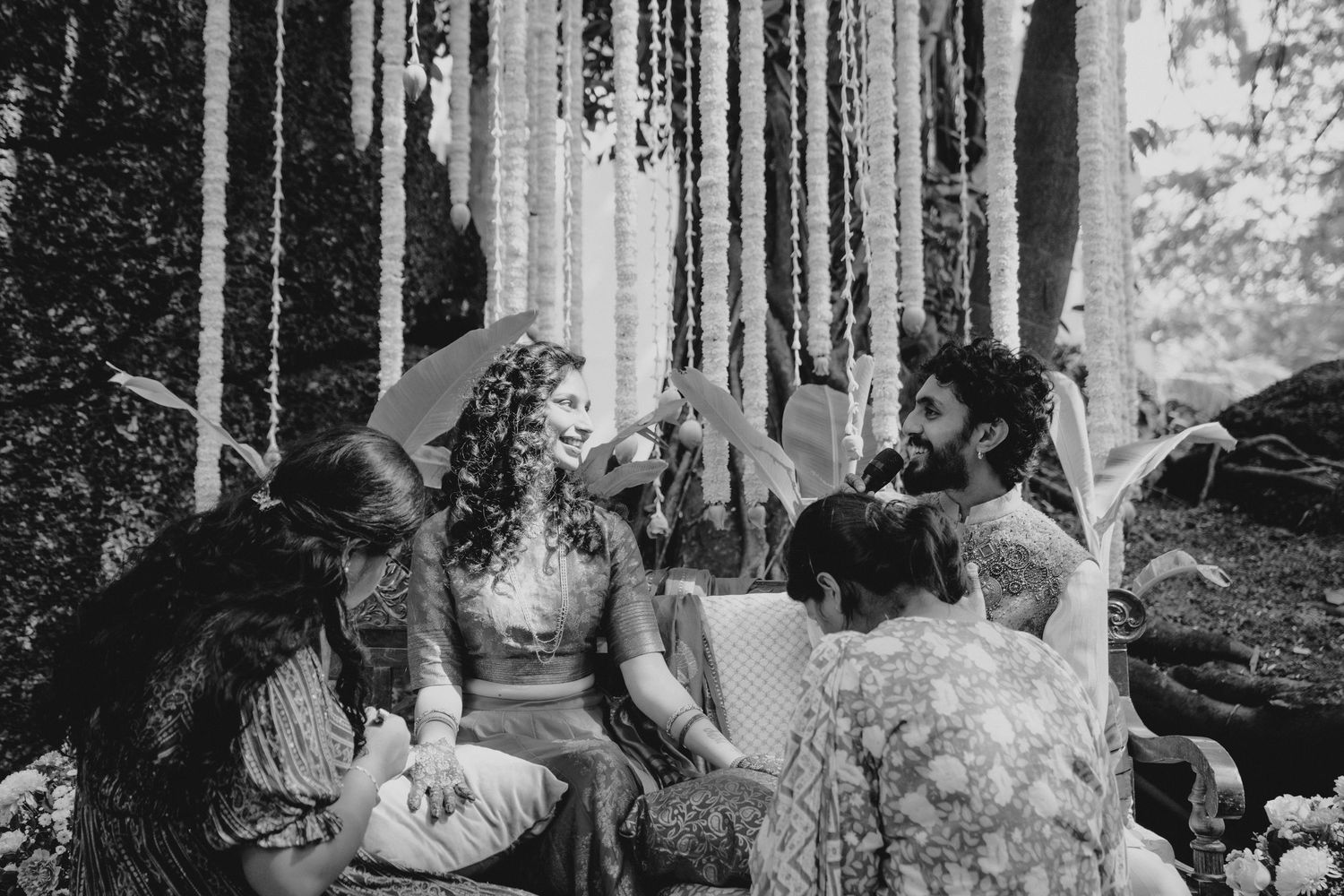 Black and white photo of a bride surrounded by friends during an outdoor bohemian wedding ceremony with ribbon decor.