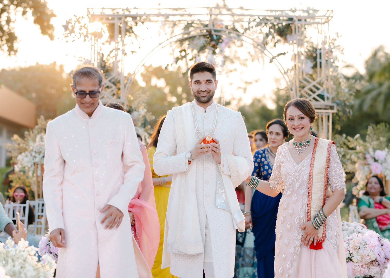 Family members dressed in traditional South Asian attire pose together during an outdoor celebration at sunset.