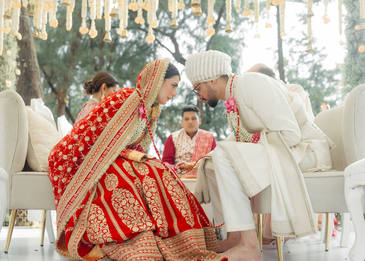 Traditional Indian wedding ceremony outdoors with bride in red sari and groom in white sherwani during ritual moments.