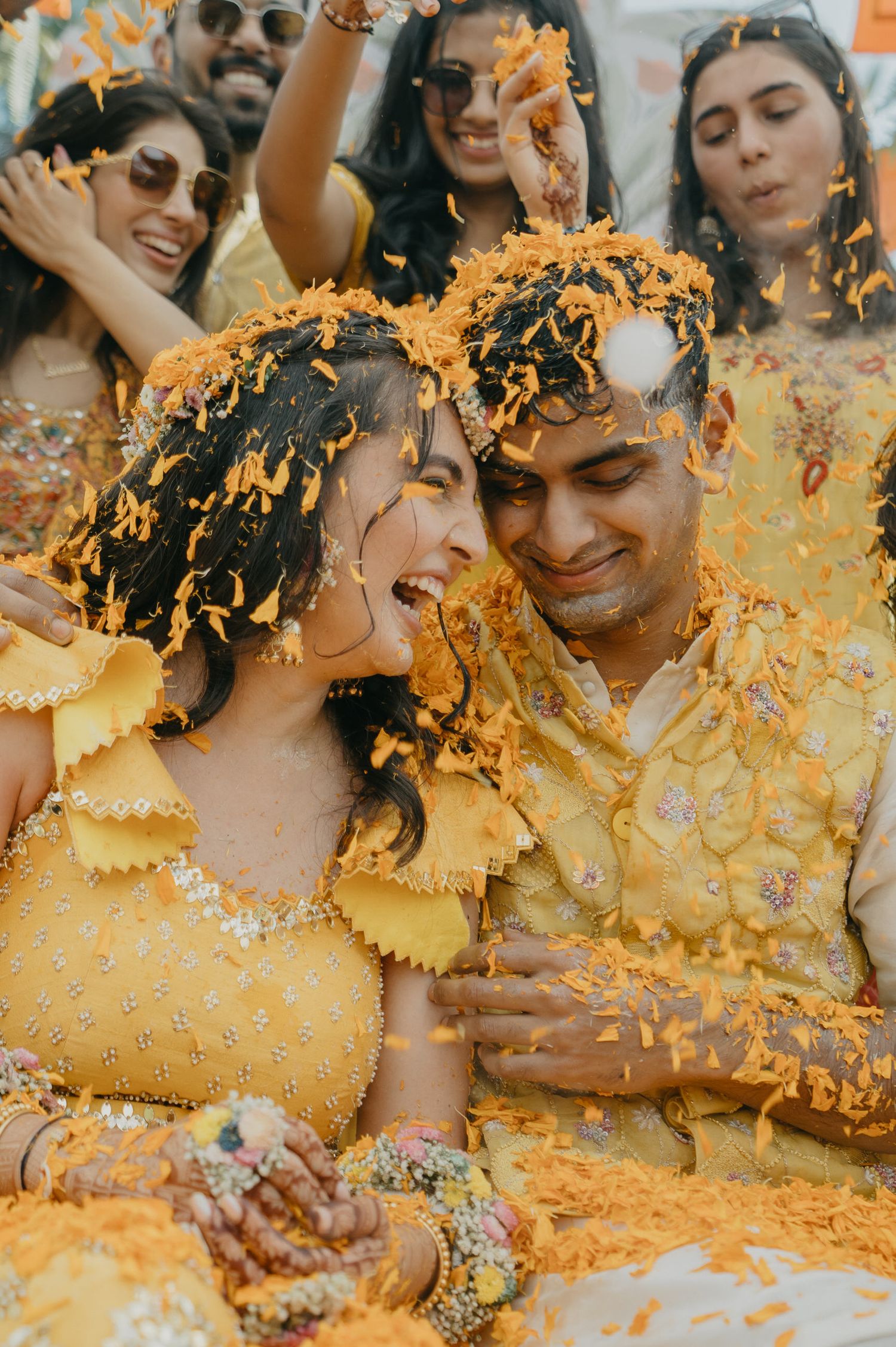 A joyful couple in yellow outfits playfully celebrate while being showered with yellow flower petals in a romantic photo series.