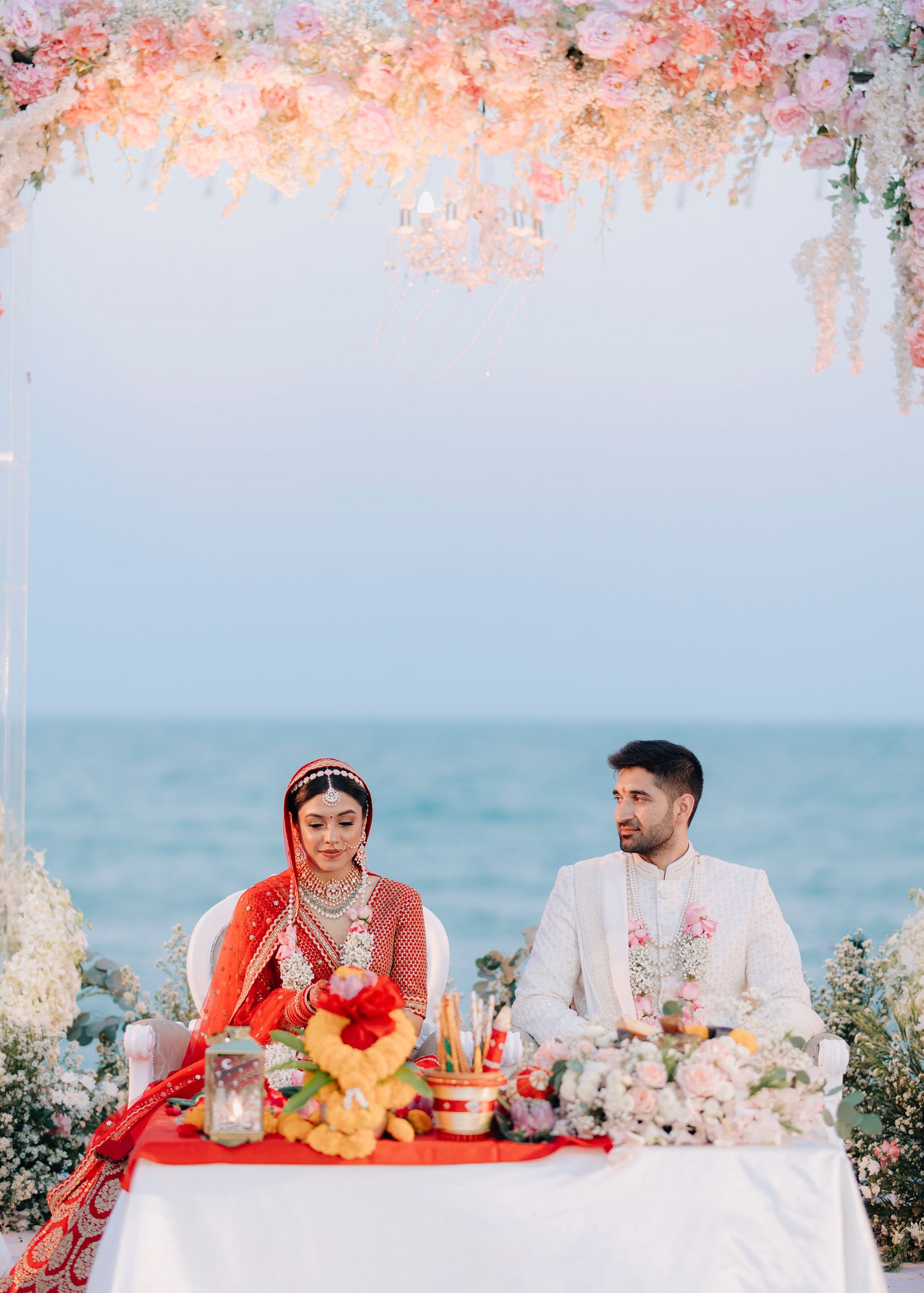 Elegant outdoor wedding ceremony setup by the ocean with pink cherry blossoms and white floral decorations.