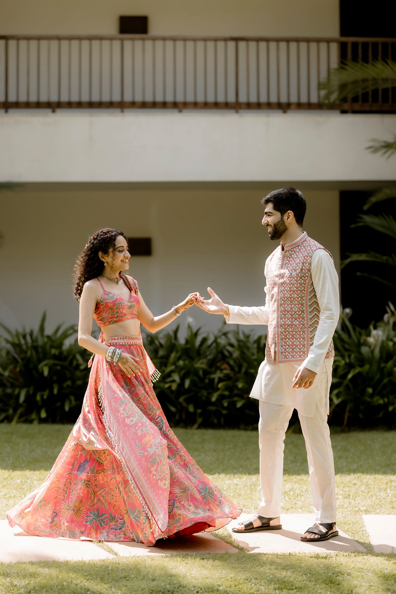 Couple in traditional Indian attire dancing together on a sunny lawn.