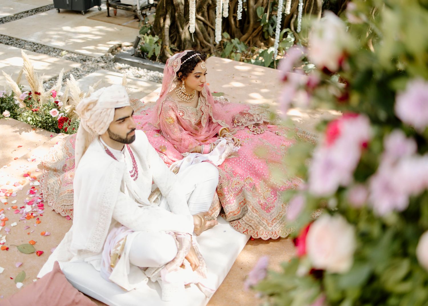 Wedding couple in traditional Indian attire posing with pink floral decorations.