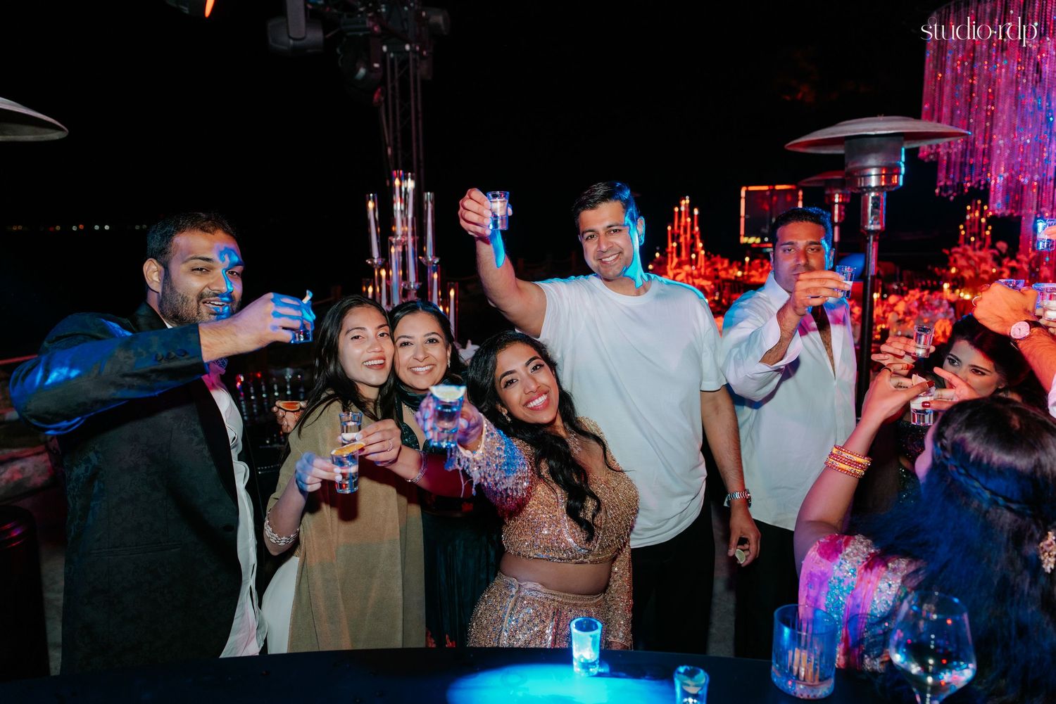 Group of friends toasting drinks at a vibrant night party with colorful lights in the background.