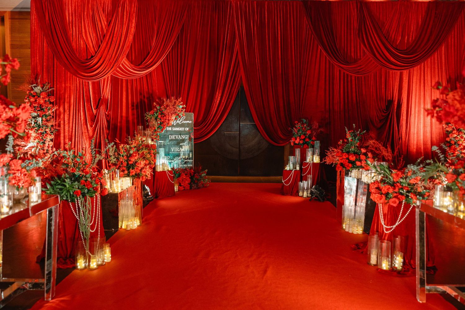 Elegant red wedding aisle with velvet drapes, floral arrangements, candles, and a glowing ice sculpture centerpiece.