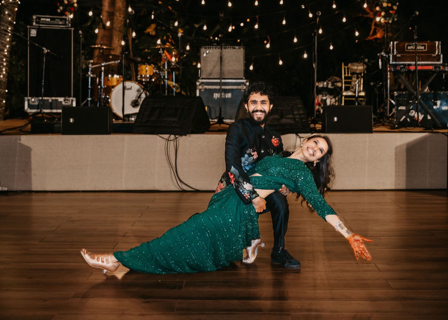 Couple in elegant attire performing a dramatic dance dip on a wooden floor at a festive evening event.