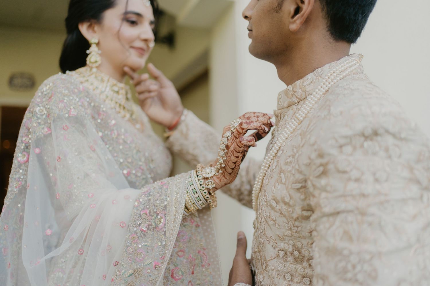 A tender moment between a couple in traditional Pakistani wedding attire with intricate white and gold embroidered outfits.