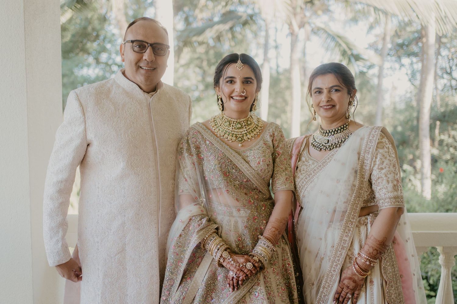Wedding party in traditional cream and gold South Asian attire pose together in outdoor garden setting with bright sunlight.