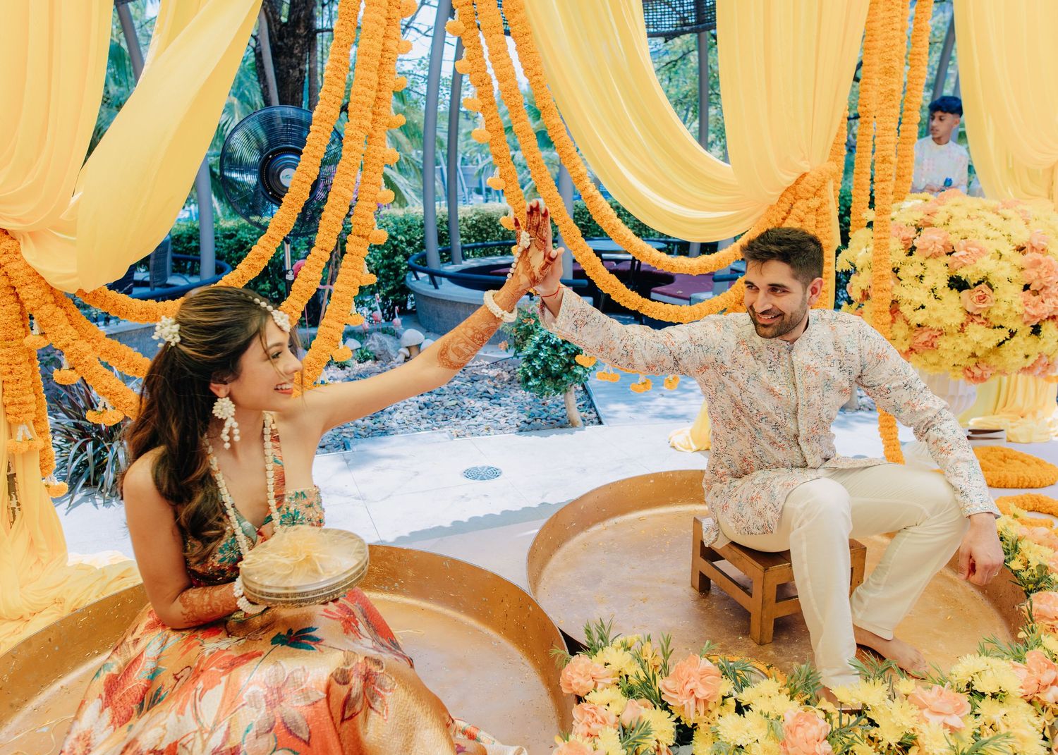 Traditional Indian pre-wedding ceremony setup with yellow and orange drapes creating a vibrant mandap decorated with flowers.