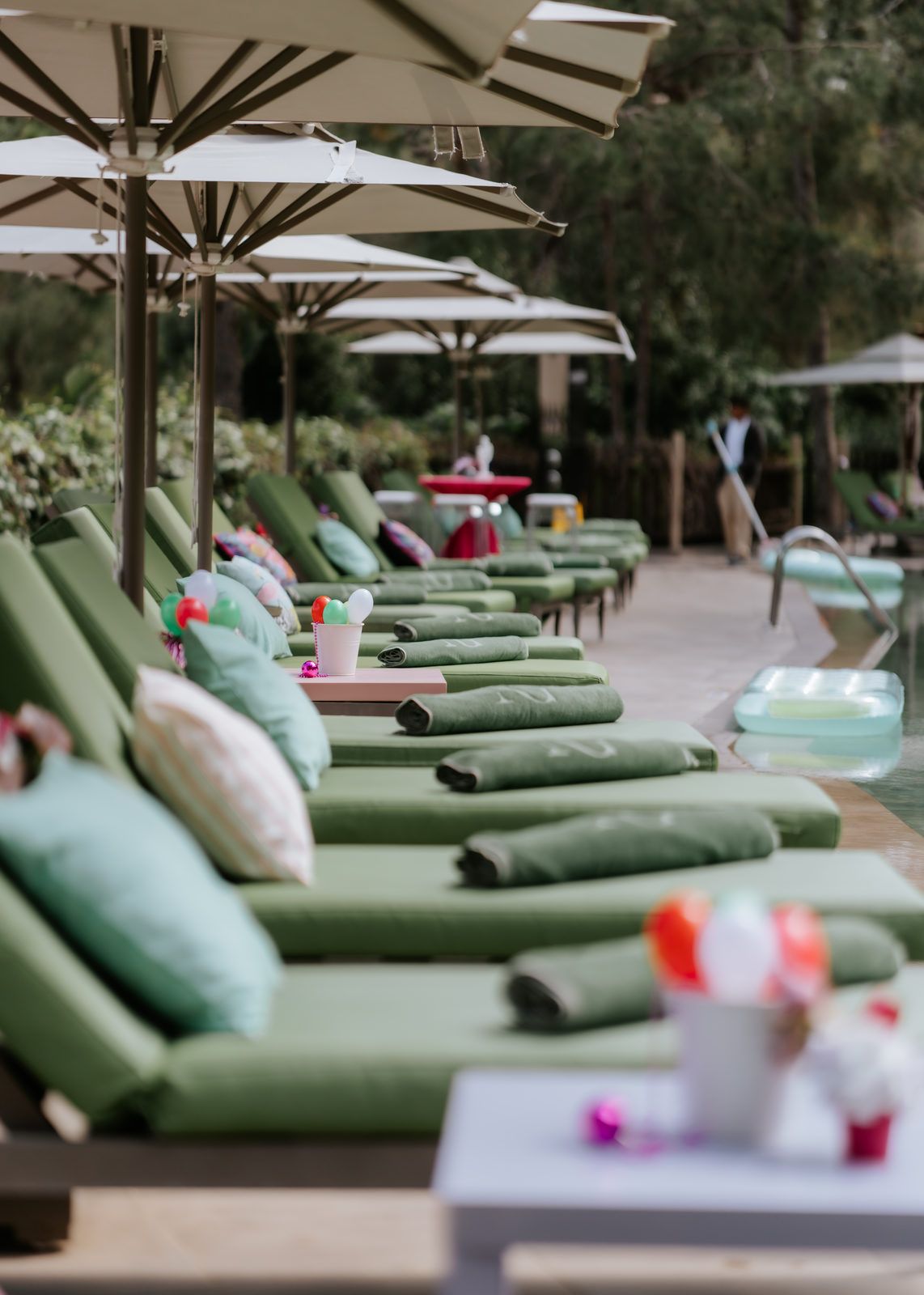 Luxury poolside lounge chairs with green cushions and white umbrellas at an upscale resort.