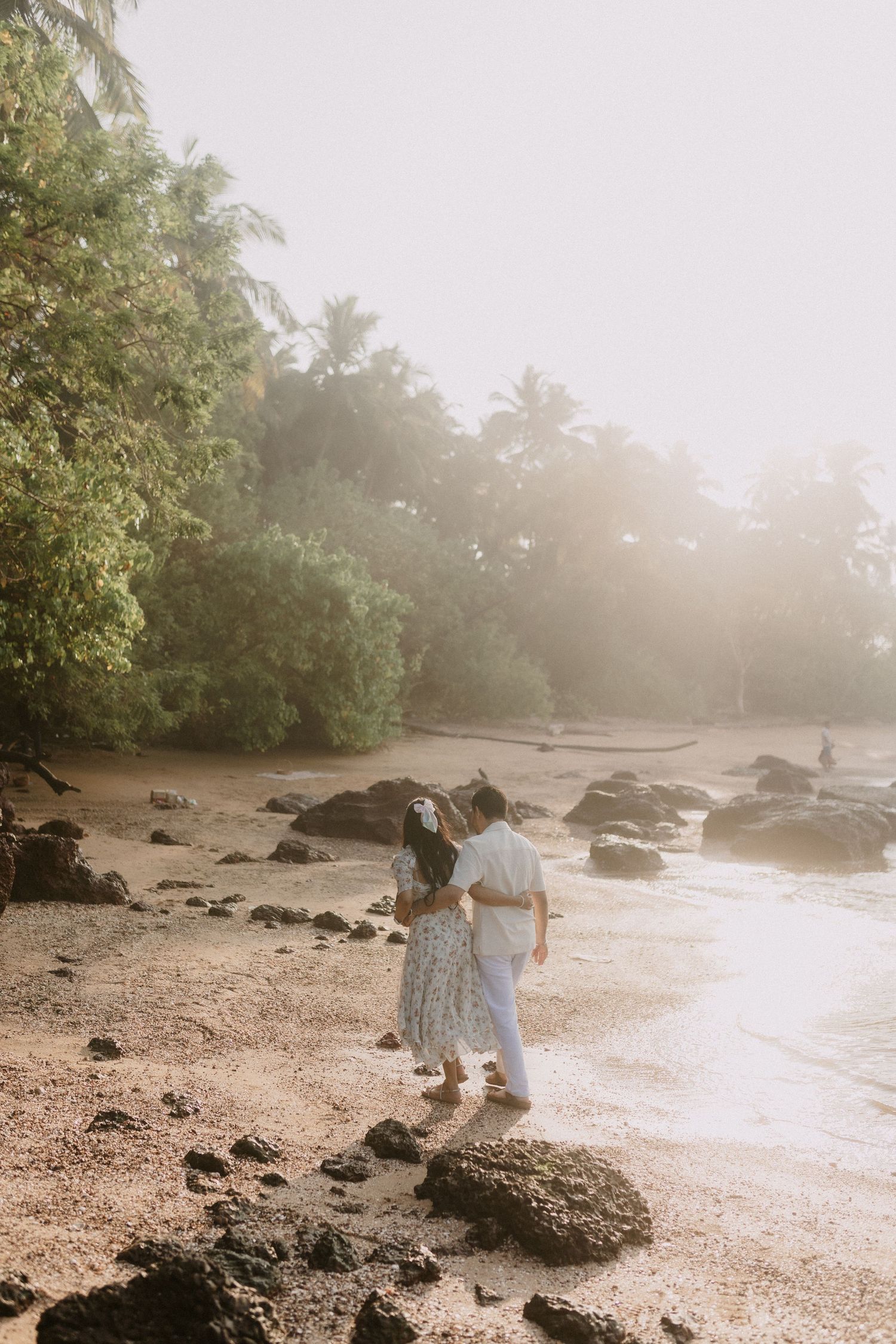 Two figures explore a misty rocky beach at sunset as golden light filters through the trees and creates a dreamy atmosphere.